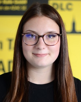 Junge Frau mit langen braunen Haaren und Brille lächelt vor gelbem Hintergrund